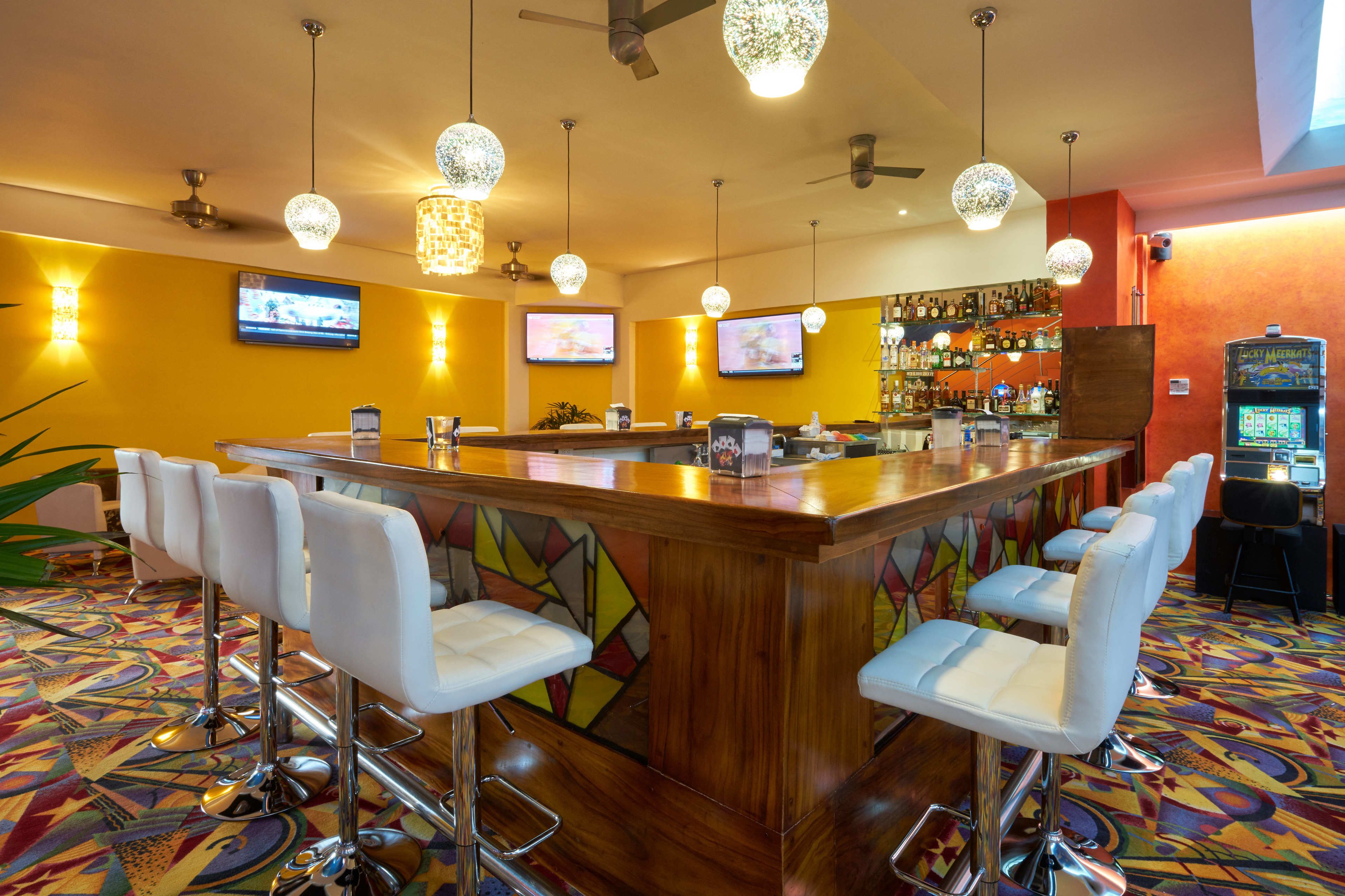 A bar area with a wooden counter, white bar stools, and multiple screens.