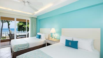 A hotel room with two beds, a ceiling fan, a nightstand with a lamp, and a view of the ocean.
