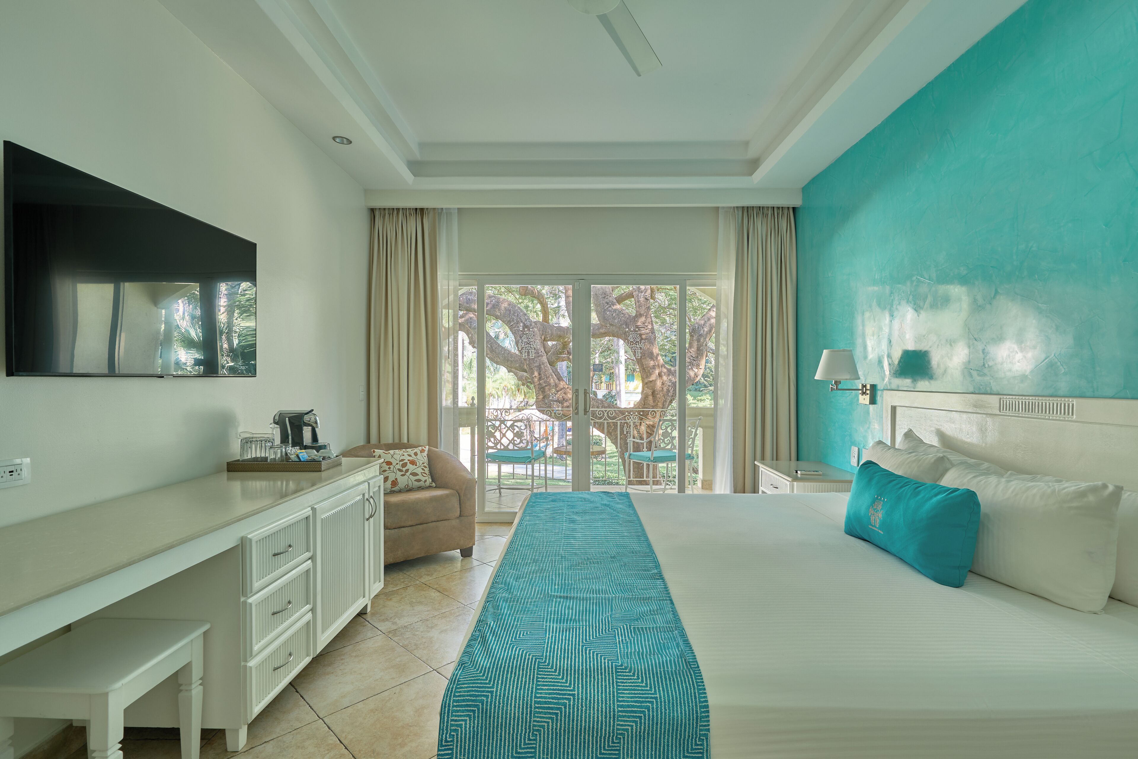 A hotel room with a bed, a desk, a chair, a TV, and a view of the outdoors.