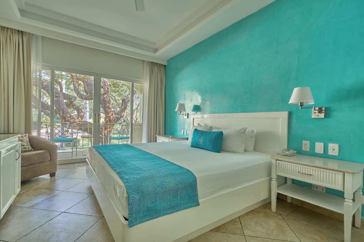 Une chambre d’hôtel avec un grand lit, une table de chevet, une lampe, une chaise et une vue sur l’extérieur.