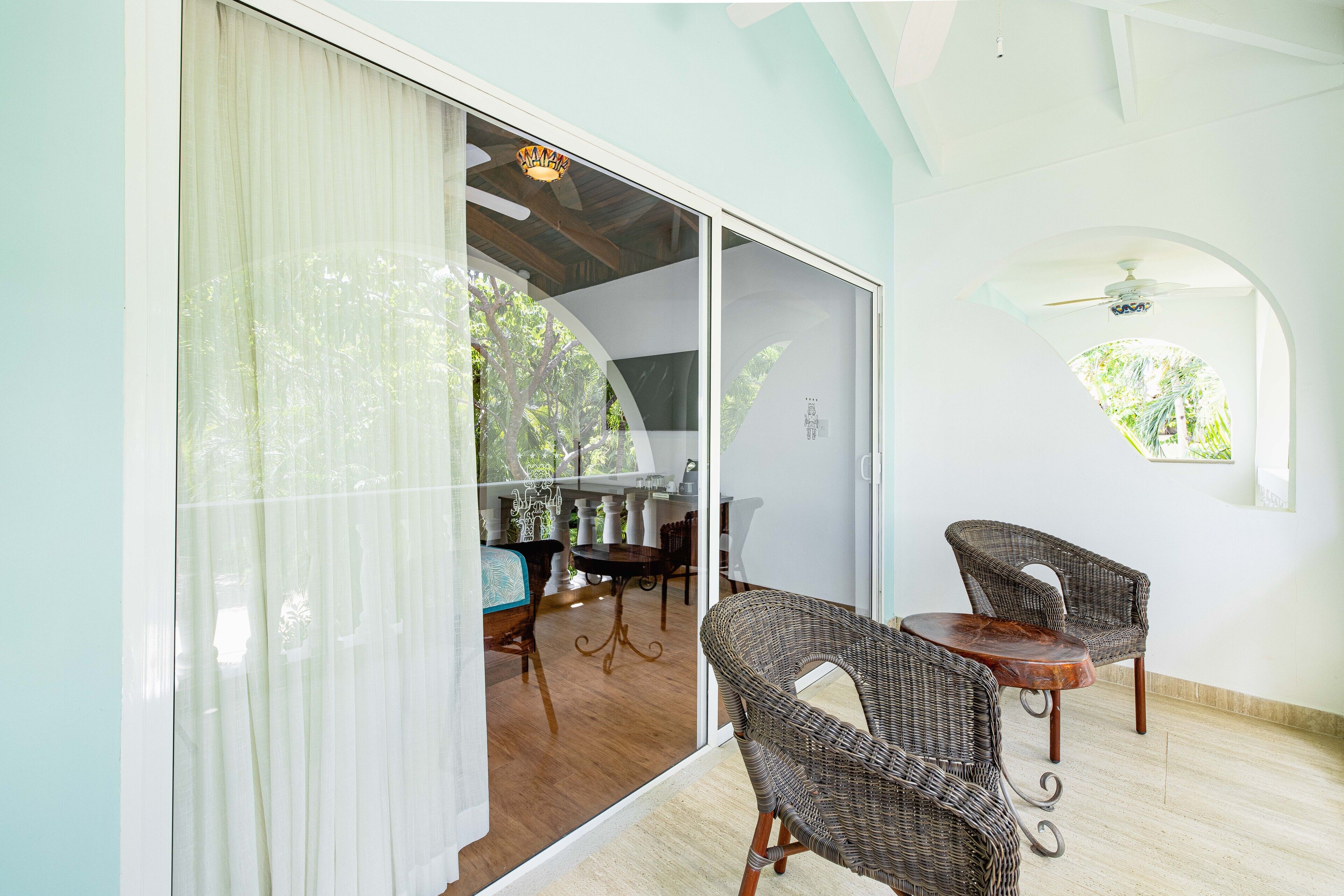 A room with a dining area, wicker chairs, a table, and a view through a glass door.