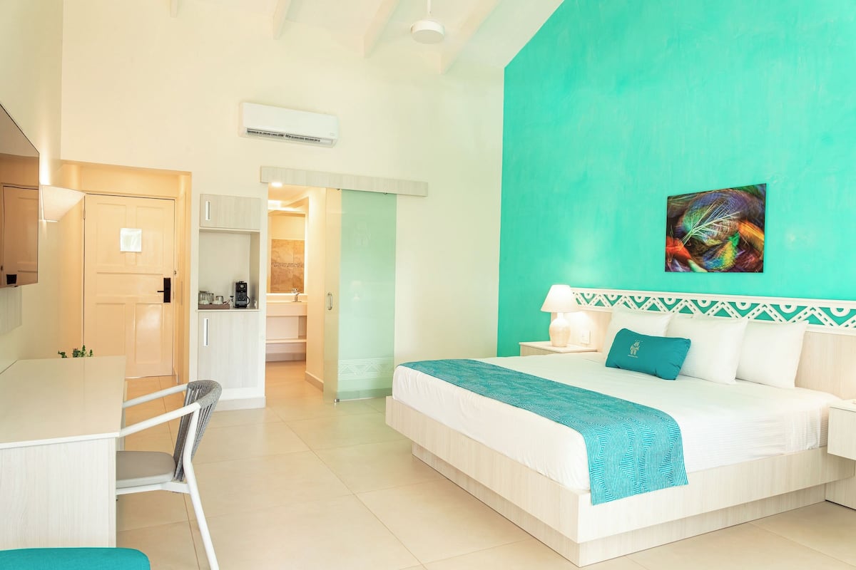 Une chambre d’hôtel avec un lit, un bureau et une chaise. On aperçoit une salle de bain au fond.