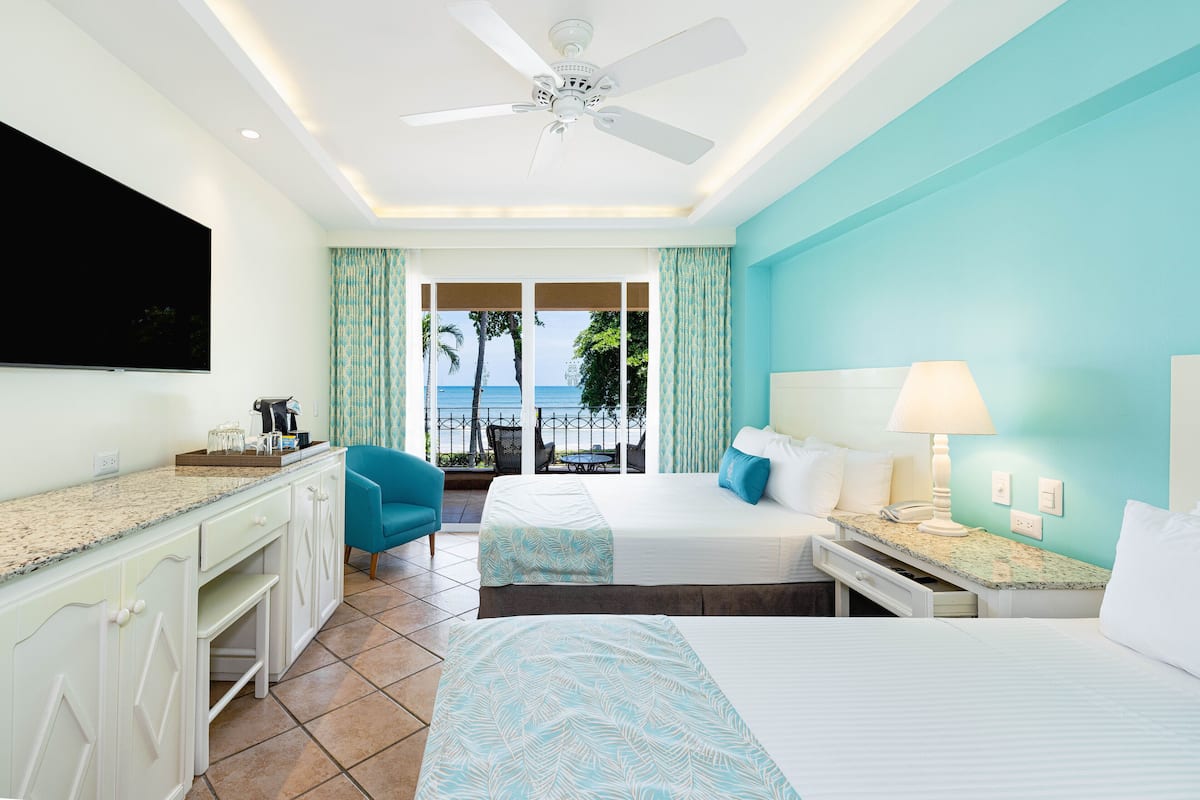 Une chambre d’hôtel avec un balcon, un ventilateur de plafond, une télévision et un lit recouvert d’une courtepointe à motifs.