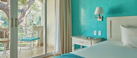 A hotel room with a bed, a nightstand, a lamp, a chair, and a view of a garden through a glass door.