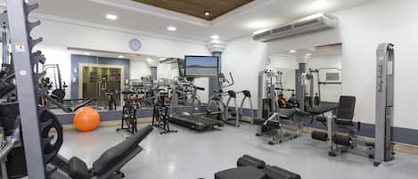 A gym with various exercise equipment, a large mirror, and a television screen.