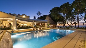 Ein Poolbereich mit Bar, Liegestühlen und einer strohgedeckten Struktur.