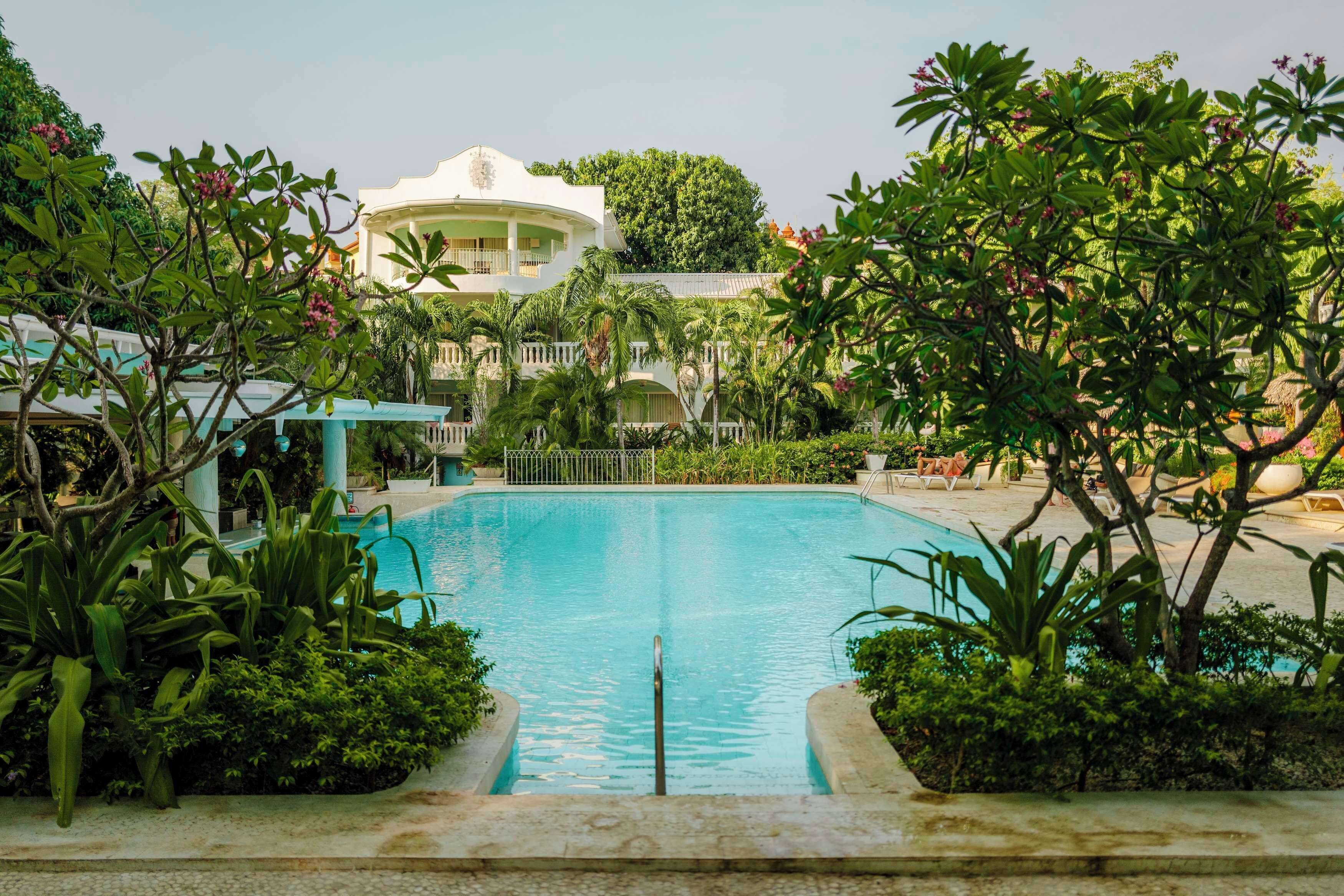 A swimming pool surrounded by lush greenery and a white building with balconies.