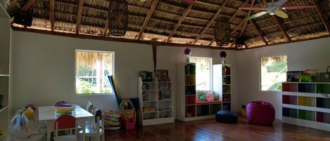 Una habitación amplia con techo de paja, suelo de madera y una gran estantería llena de libros y juguetes.
