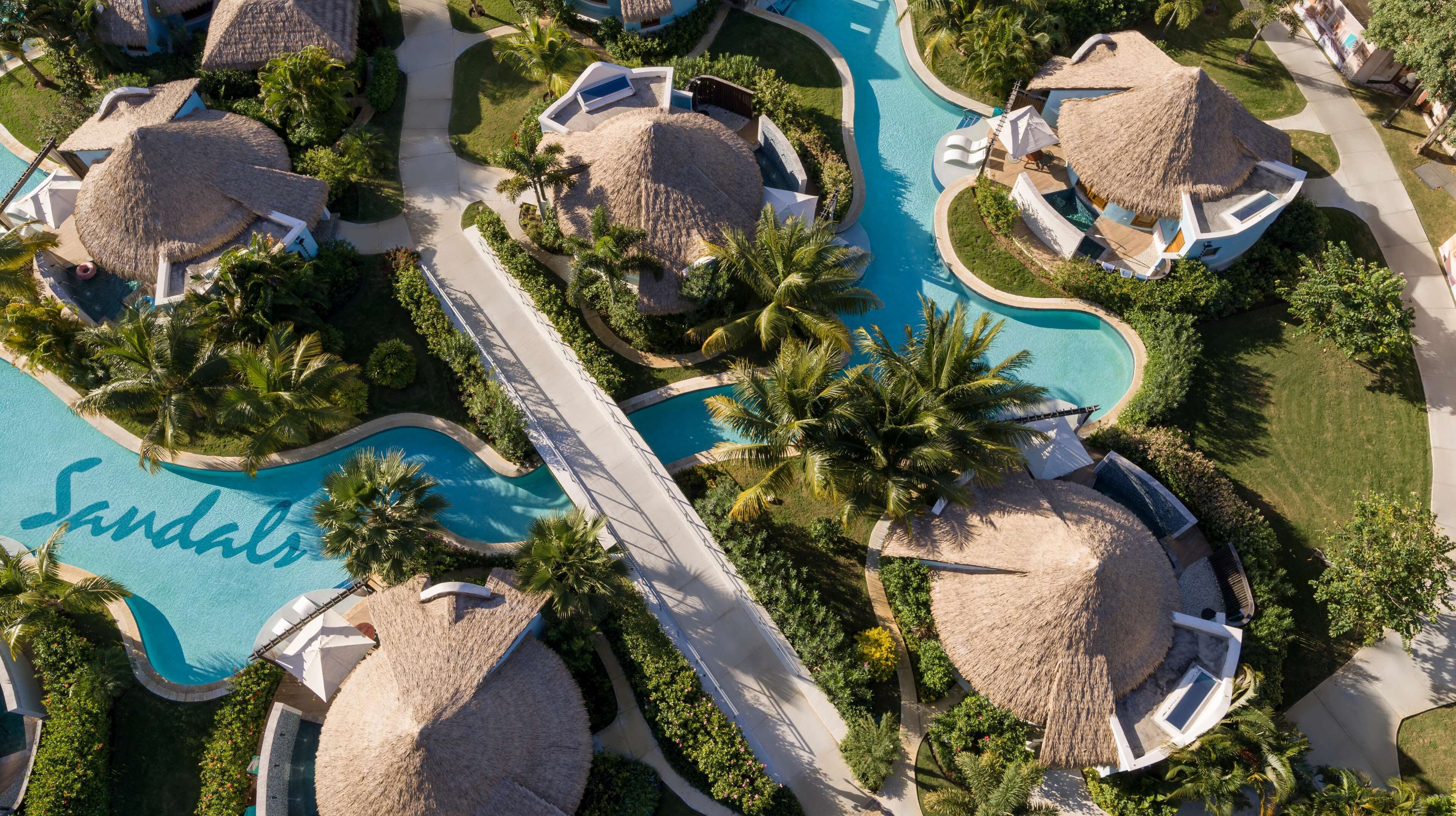 An aerial view of a resort with multiple thatched-roof structures, a central swimming pool, and well-maintained landscaping.