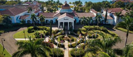 A large, white building with a central dome and columns, surrounded by palm trees and a well-maintained garden.
