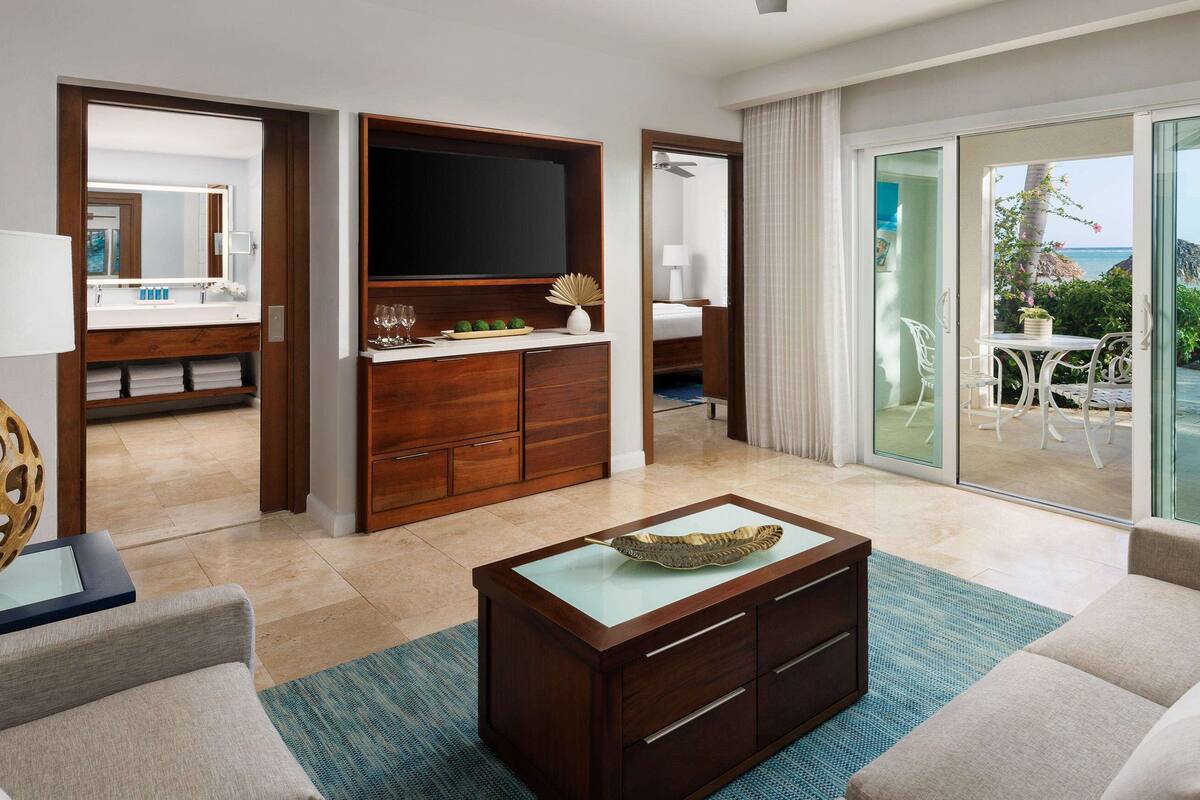 Een hotelkamer met een grote televisie, een houten kast, een bank en uitzicht op de oceaan door de schuifdeur.