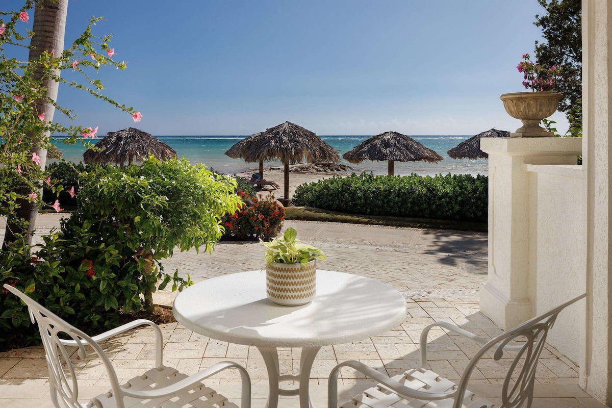 Een terras met een tafel en stoelen, een uitzicht op het strand en rieten parasols.