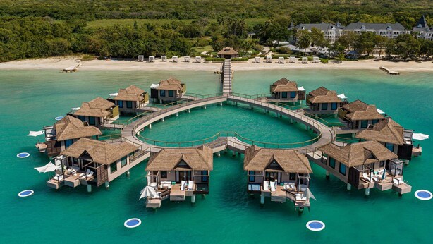 Des bungalows sur pilotis, dotés de toits de chaume, reliés par un pont, et entourés d’une eau turquoise.