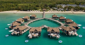 An overwater bungalows with thatched roofs, connected by a bridge, surrounded by turquoise water.
