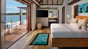 Une chambre avec un grand lit, un plancher en bois, une petite table avec des chaises, une salle de bain avec un miroir et un lavabo, et une vue sur l’eau.