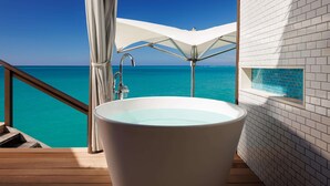 Eine Badewanne mit Blick auf den Ozean, eine weiße Fliesenwand und ein Holzboden.