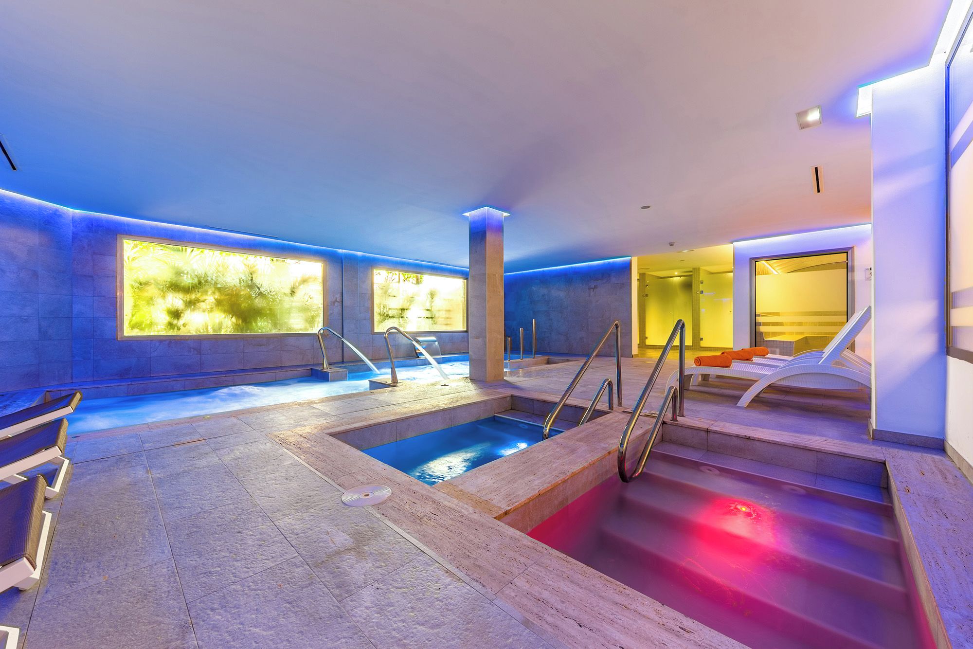 A modern indoor swimming pool with clear water, surrounded by stone walls and equipped with metal railings.