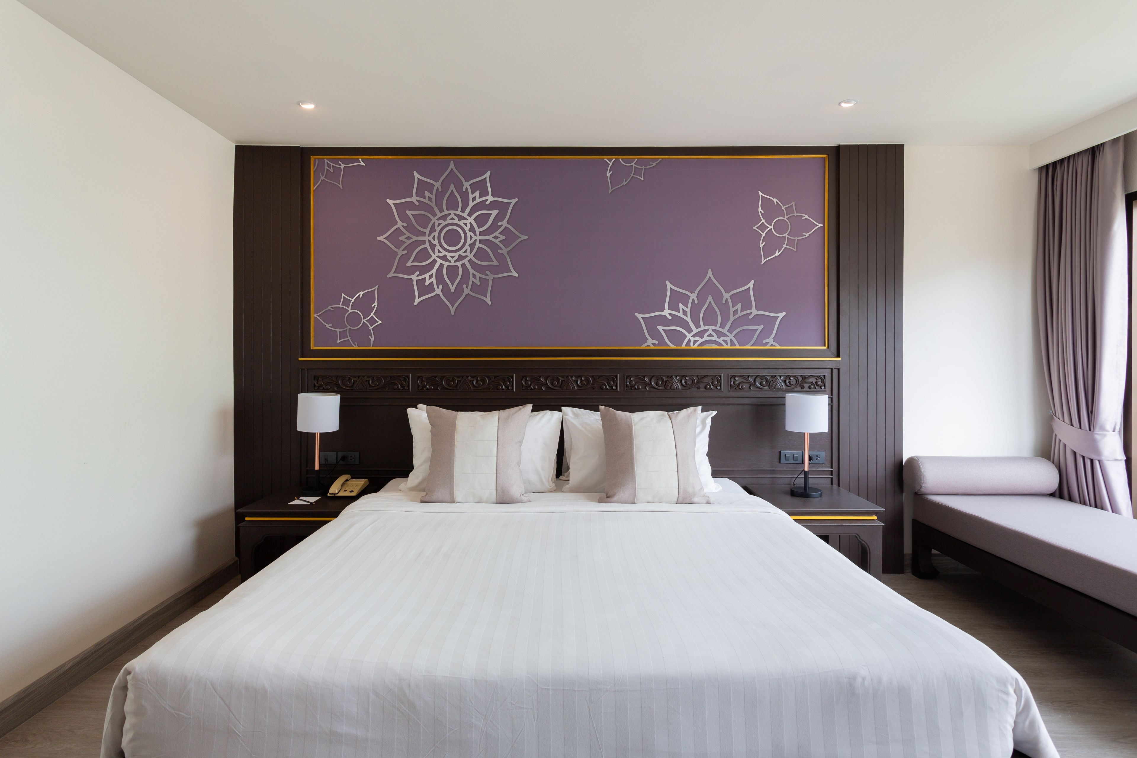 A large bed with a headboard featuring a floral design, two bedside tables with lamps, and a bench at the foot of the bed.