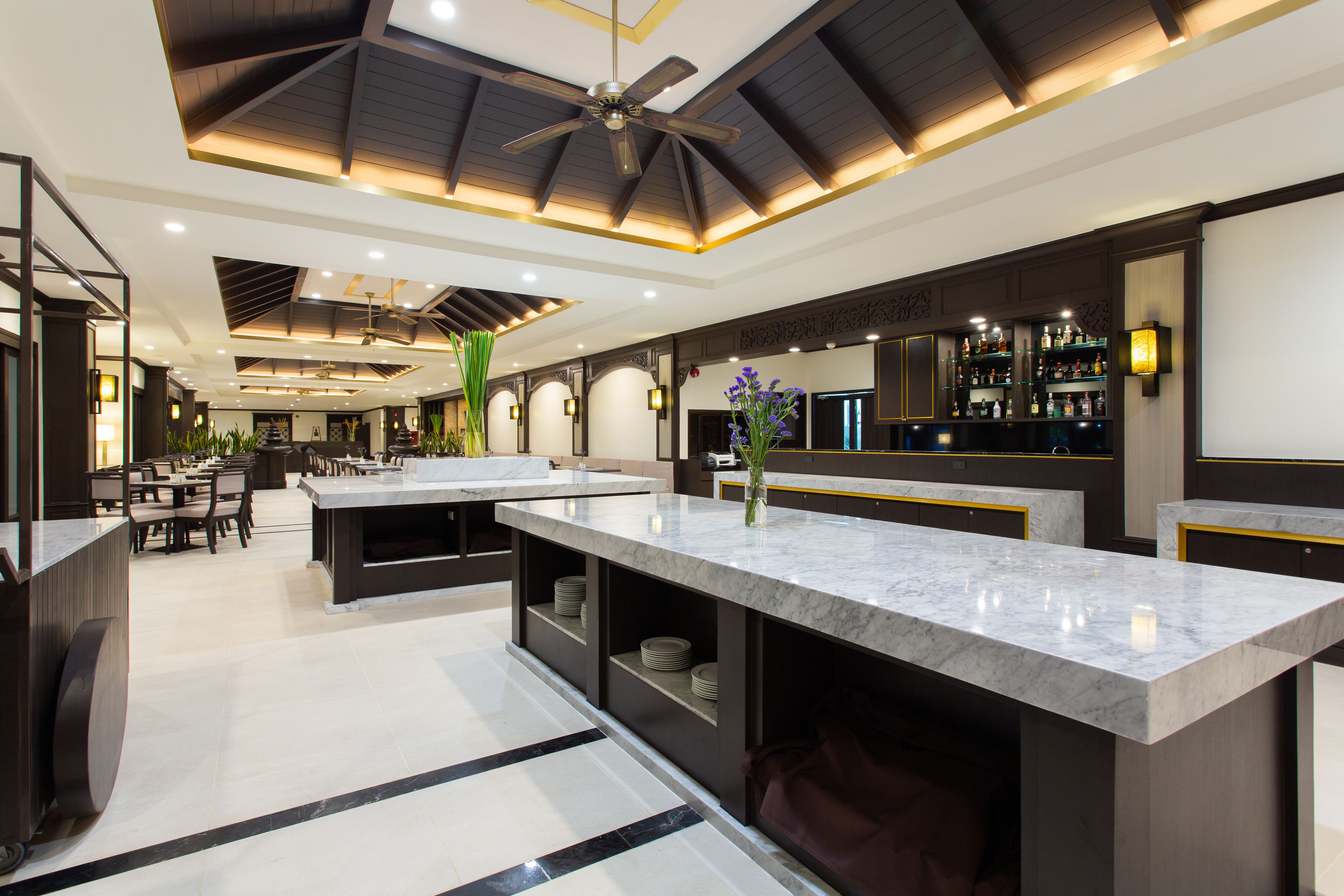 A modern kitchen with marble countertops, a central island, and a bar area with shelves of bottles.