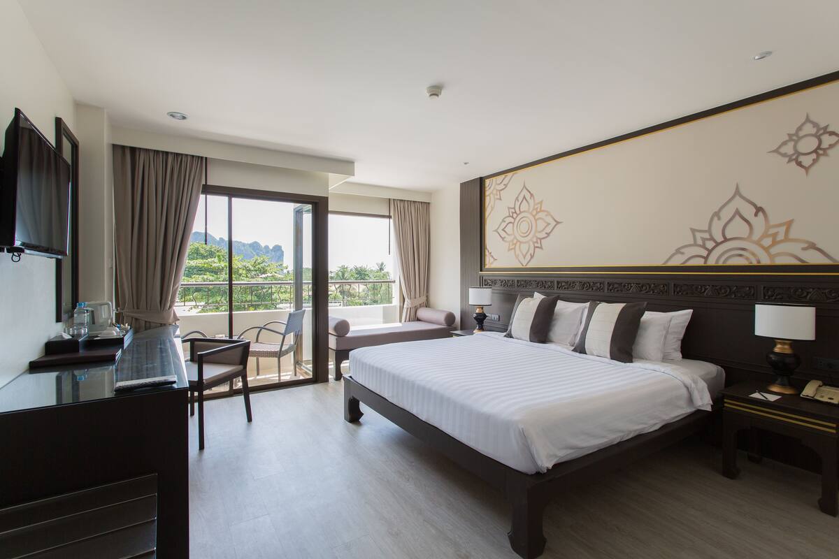Ein Hotelzimmer mit einem großen Bett, einem Schreibtisch, einem Stuhl und Blick ins Freie.