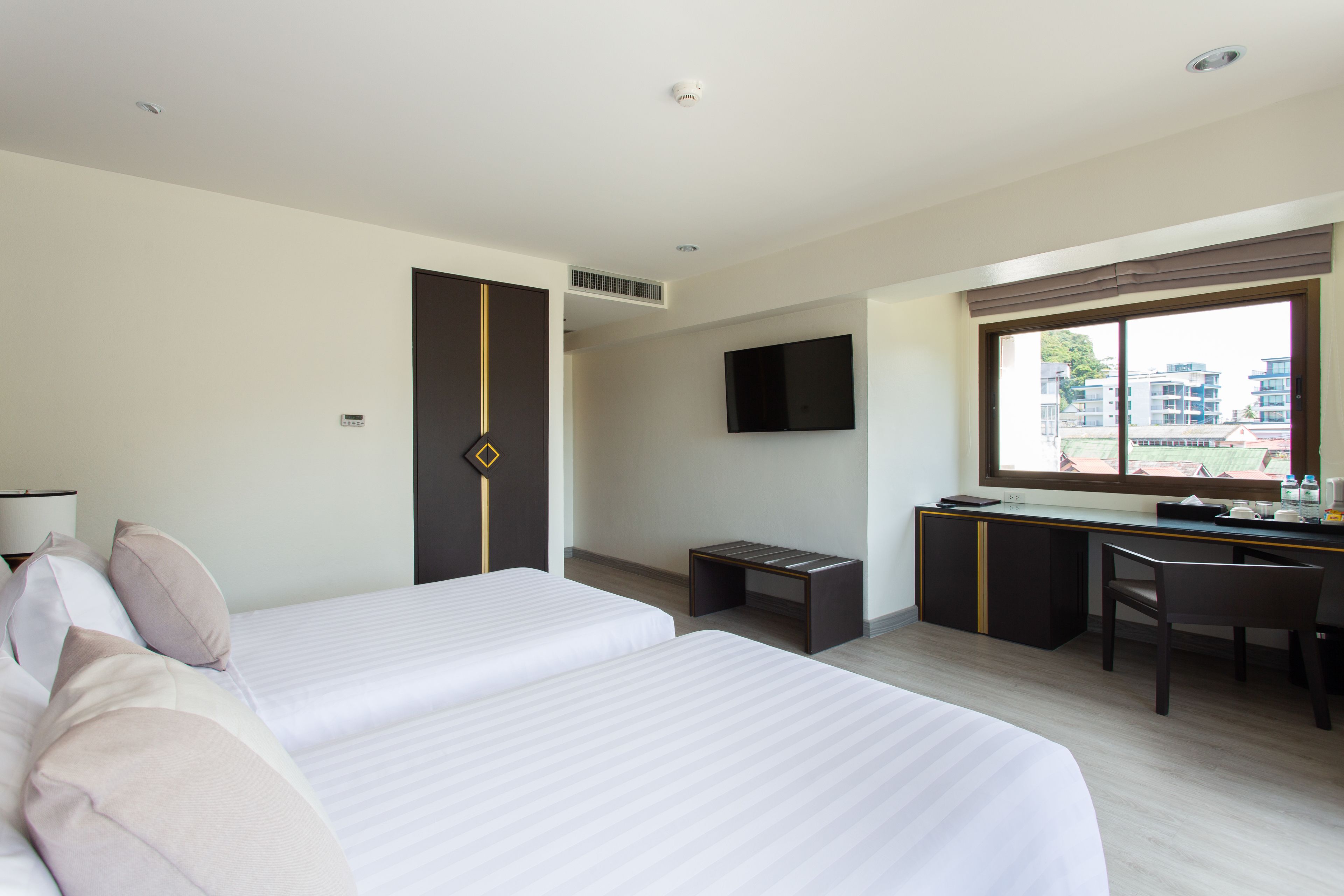 A hotel room with two beds, a desk, a chair, a TV, and a window with a city view.