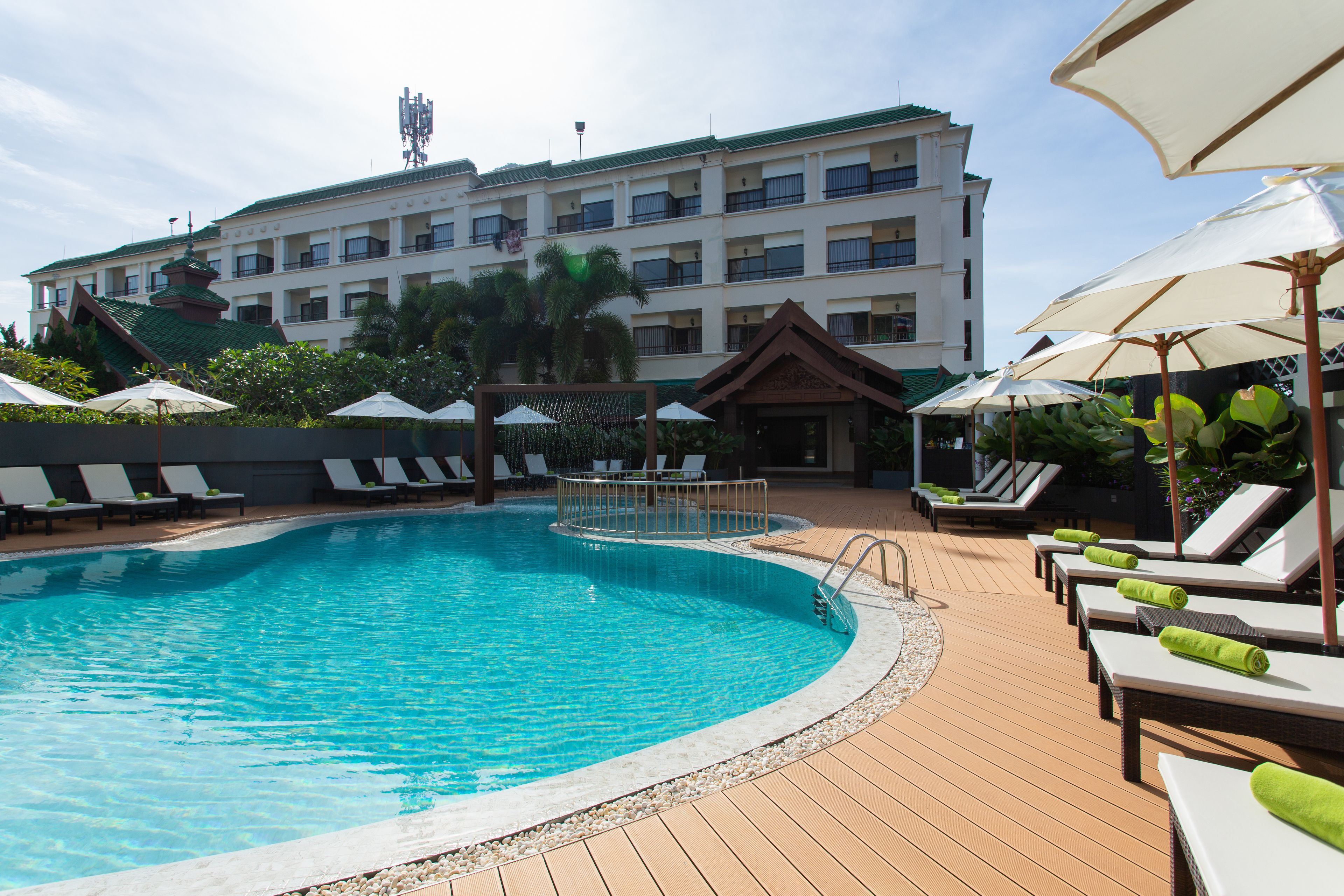 A swimming pool with lounge chairs and umbrellas, surrounded by a building with multiple balconies.