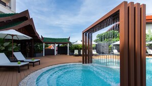A swimming pool with lounge chairs and umbrellas, surrounded by a wooden deck and a covered area with a green roof. - Krabi Heritage Hotel (Krabi)