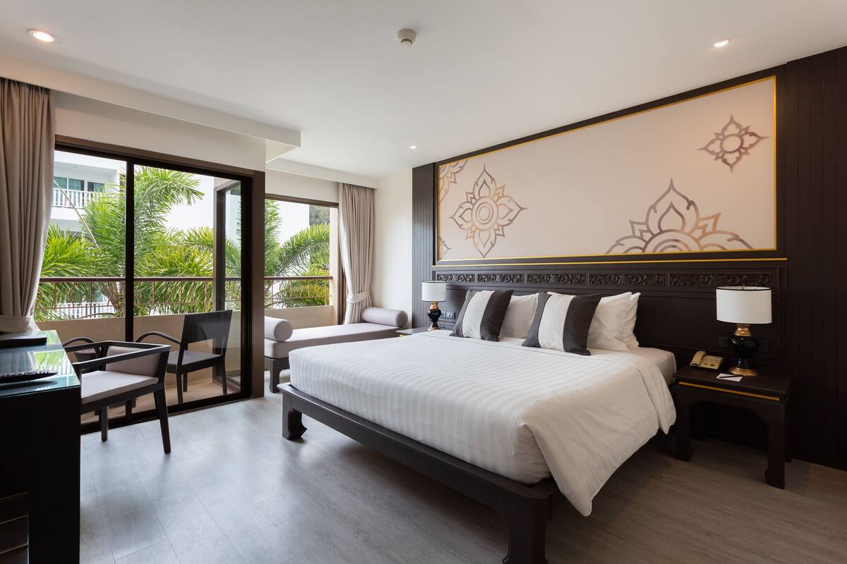 Ein Hotelzimmer mit einem großen Bett, einem Schreibtisch und einem Stuhl. Ein Fenster bietet Blick auf Grünflächen.
