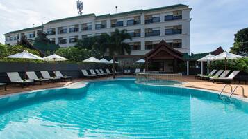 A swimming pool with lounge chairs and umbrellas, surrounded by a building with multiple balconies.