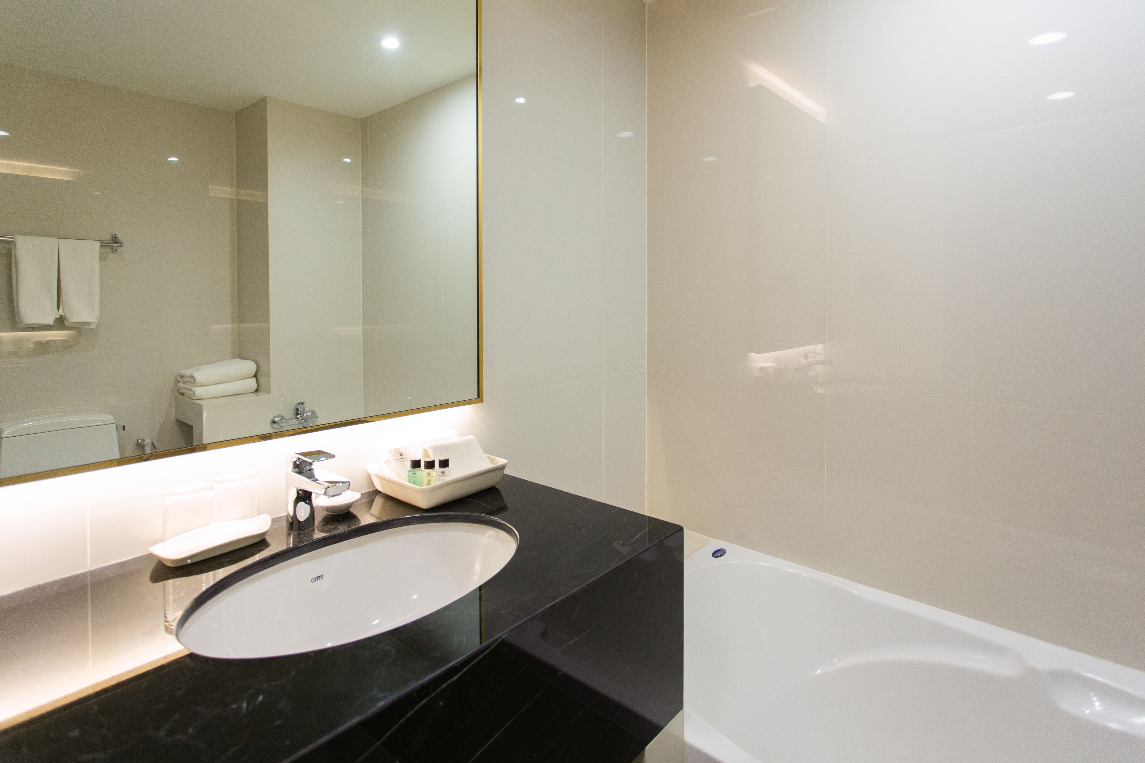 A modern bathroom with a black marble sink, a white bathtub, and a large mirror.