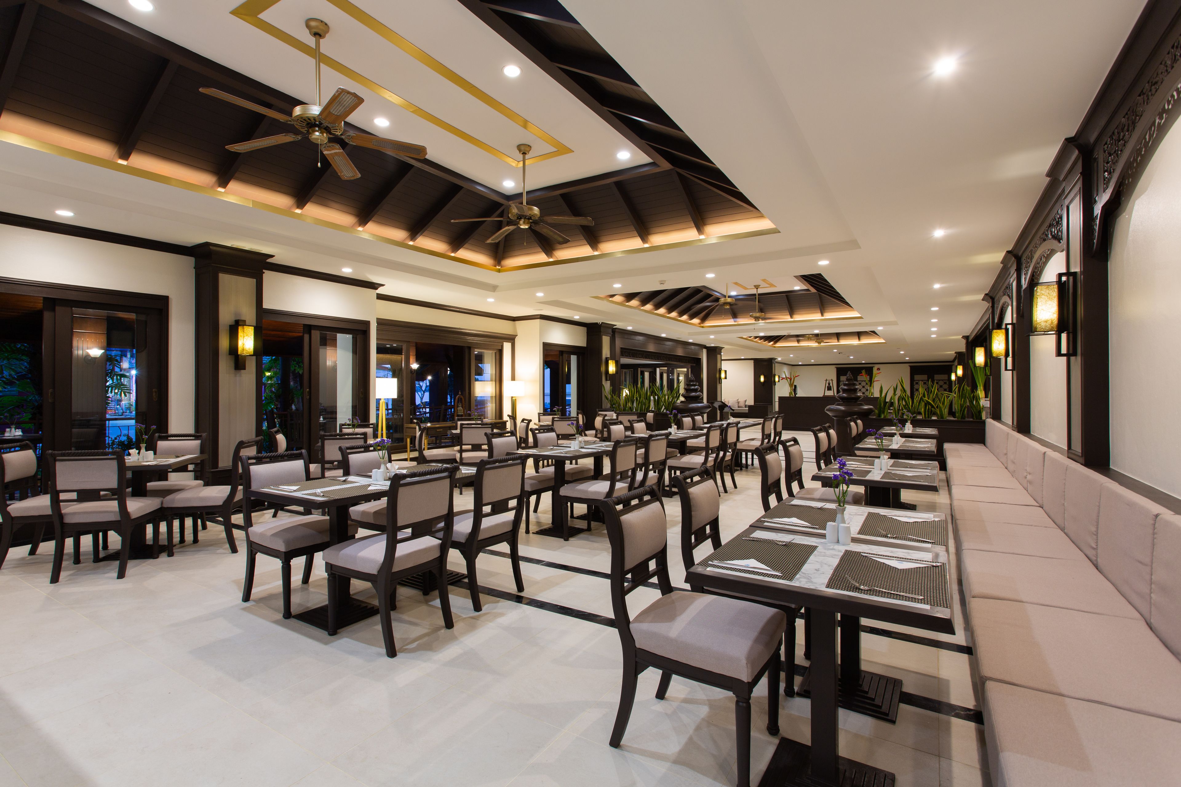 A spacious restaurant with multiple dining tables and chairs, ceiling fans, and recessed lighting.
