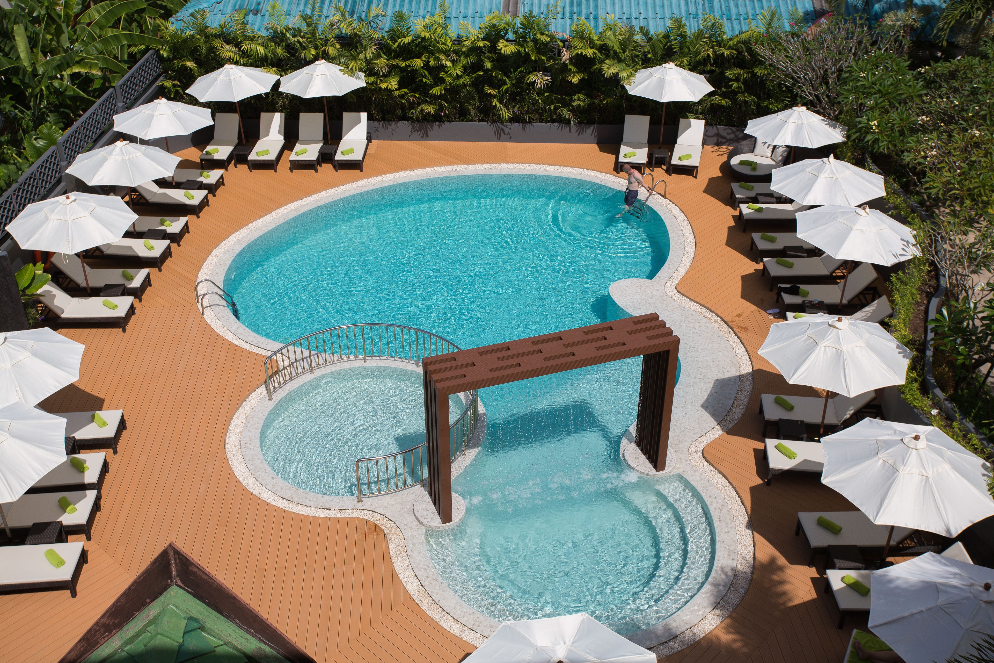 A pool area with multiple lounge chairs and umbrellas, a central pool, and a small waterfall feature.