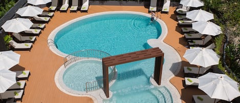 A pool area with multiple lounge chairs and umbrellas, a central pool, and a small waterfall feature.