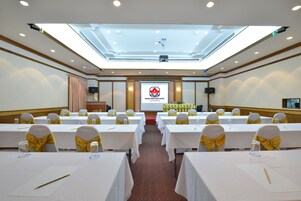 Una sala conferenze con tavoli apparecchiati per una riunione, uno schermo per presentazioni e un palco con un podio.