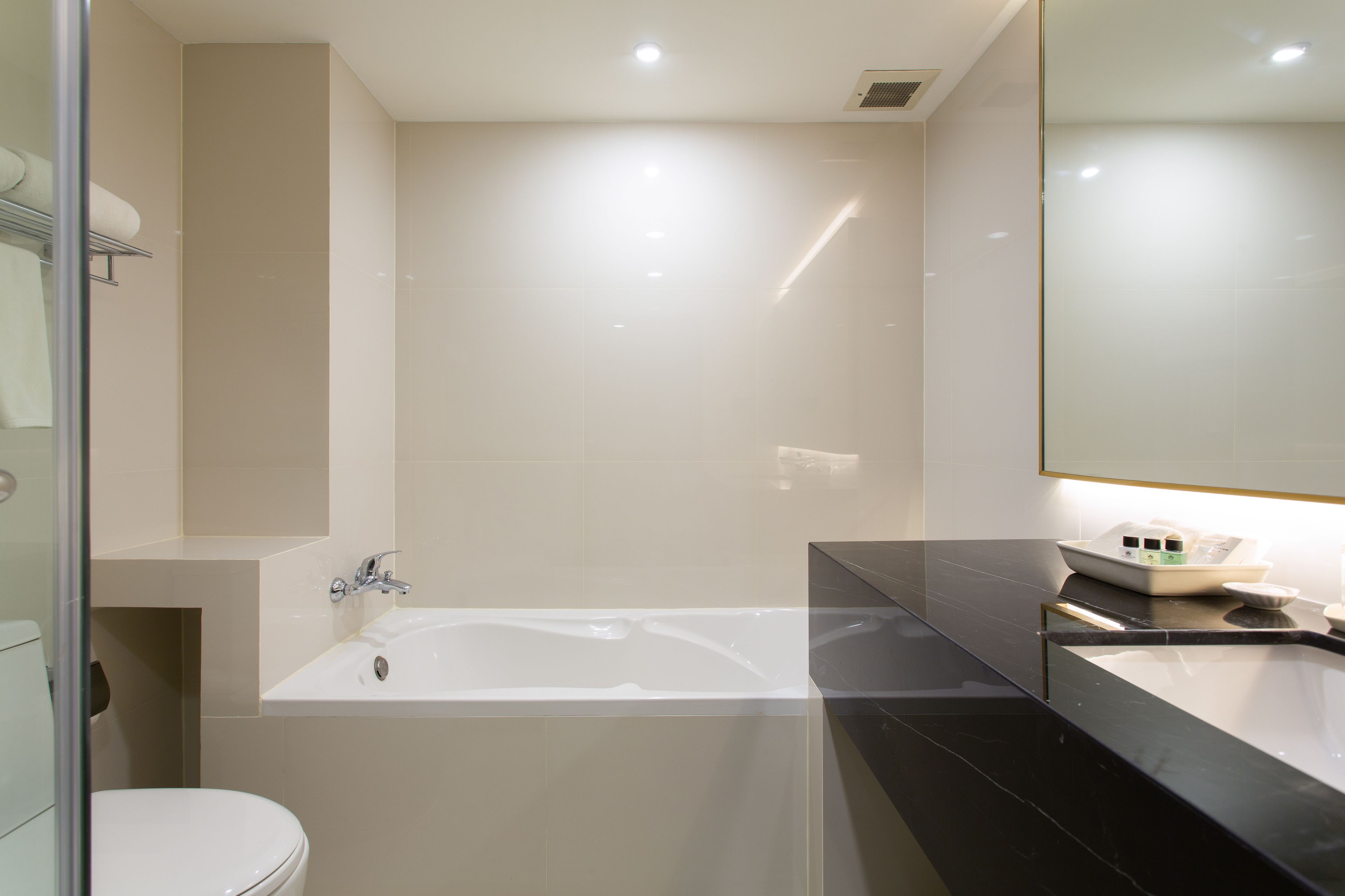 A modern bathroom with a white toilet, a bathtub, and a black sink.