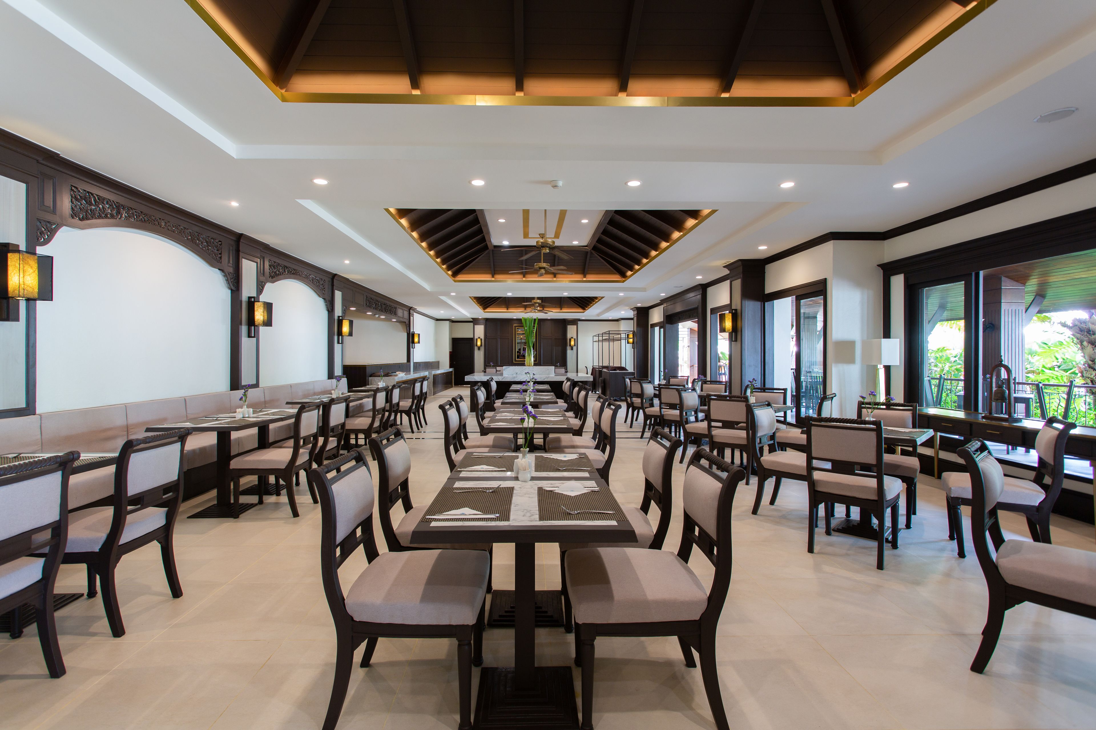 A spacious dining area with multiple tables and chairs, a ceiling fan, and large windows allowing natural light.