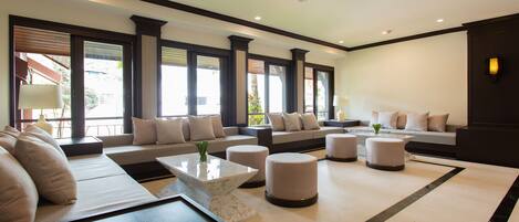 A modern living room with a sectional sofa, ottomans, a coffee table, and large windows with a view.