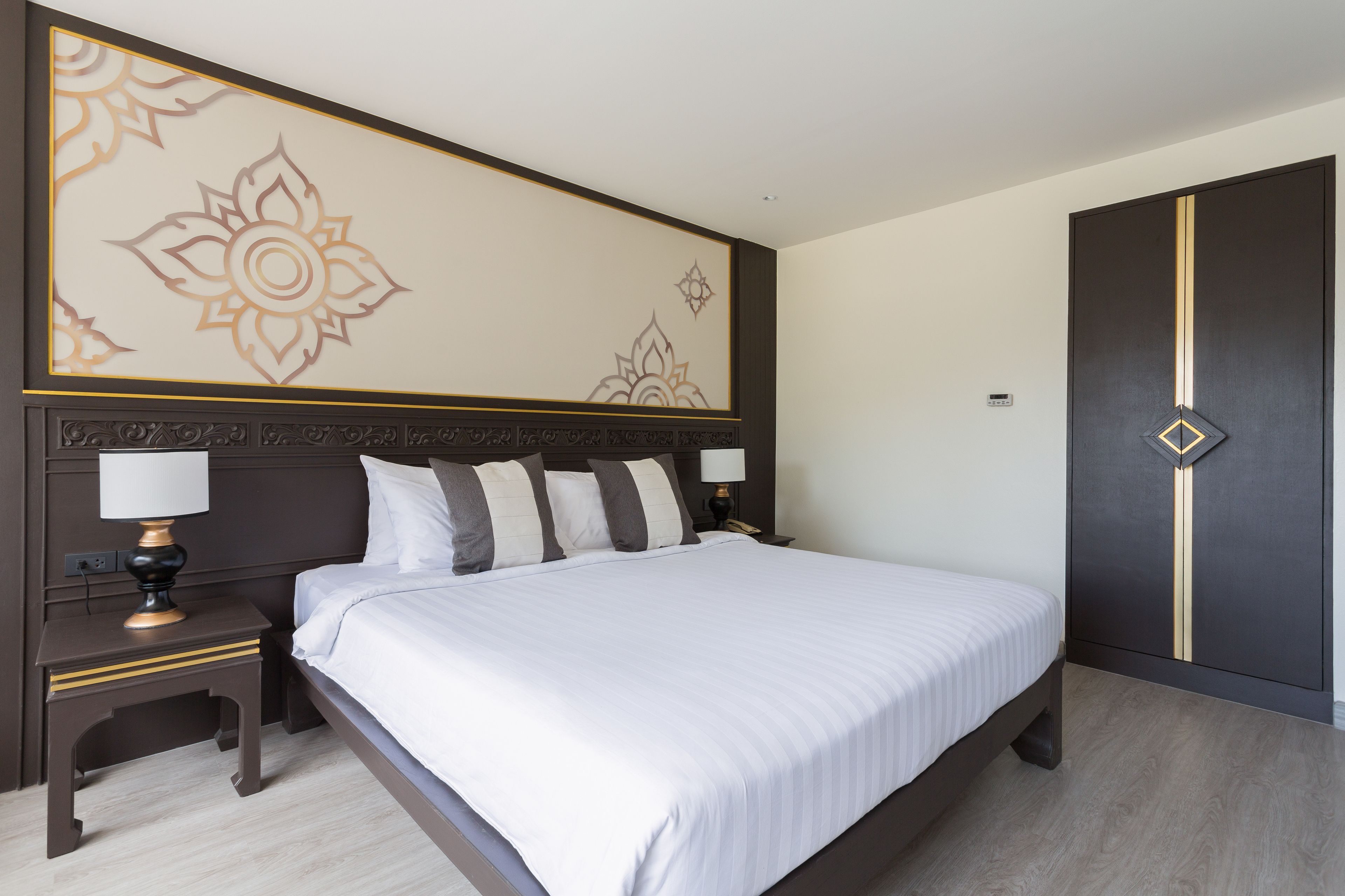 A neatly made bed with white linens, a dark wooden headboard, and a decorative wall panel.