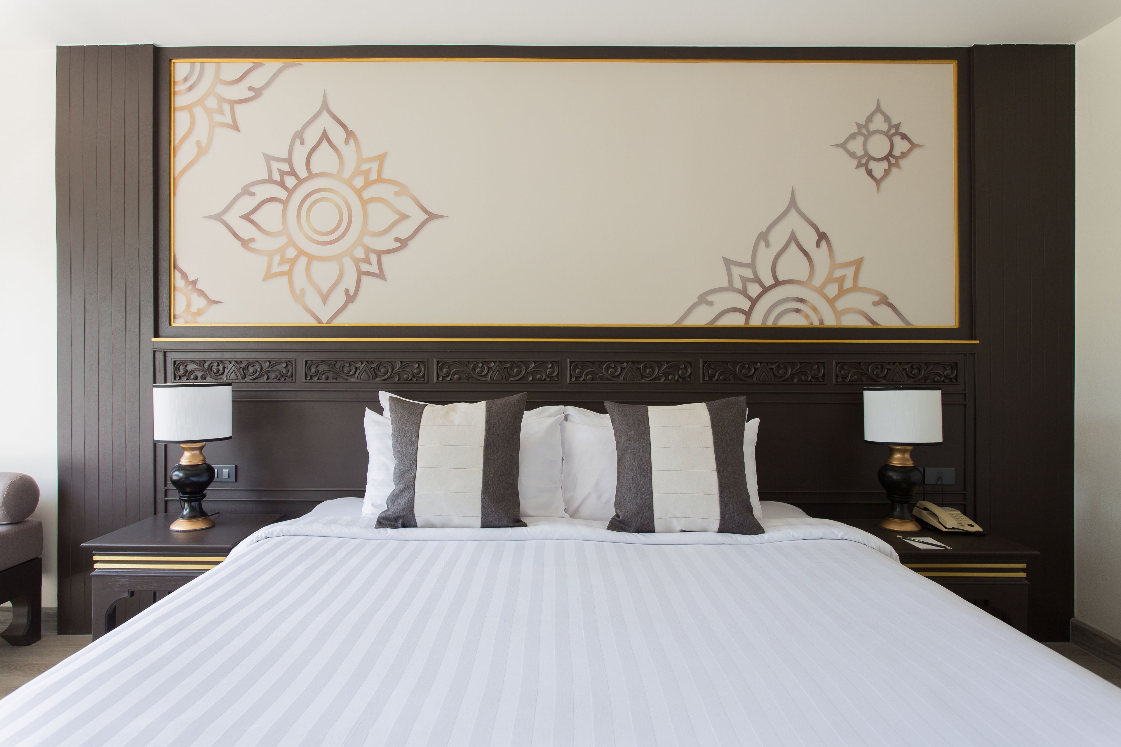 Una habitación de hotel con una cama grande, dos mesitas de noche con lámparas y un cabecero decorativo.
