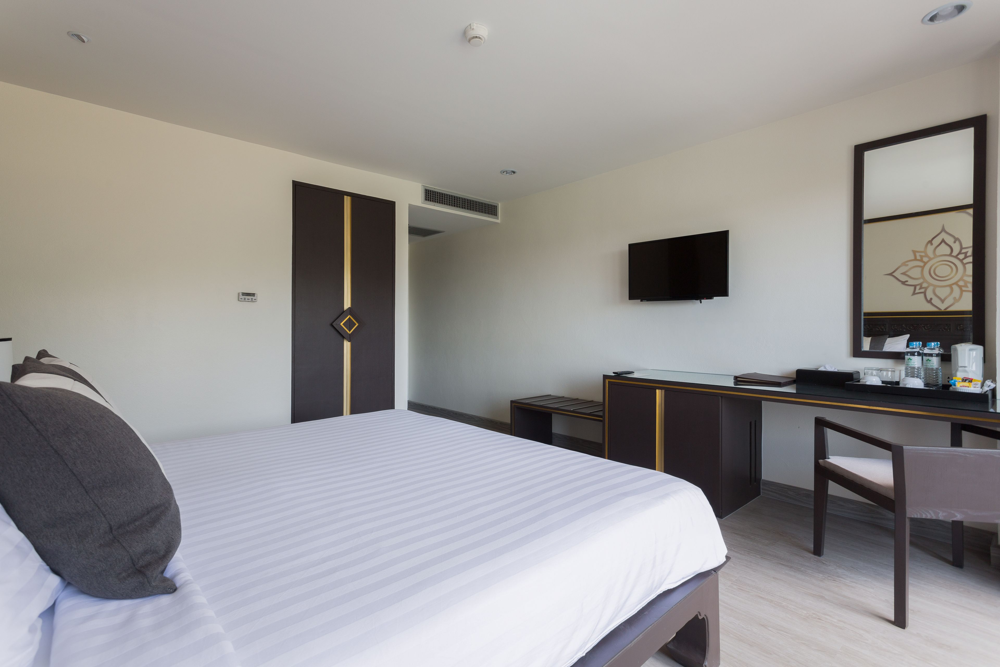 Habitación de hotel con cama, escritorio, silla, televisión y espejo.