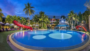 A resort pool with a red slide, palm trees, and a building with a unique roof design. - Chada Thai Village (Krabi)
