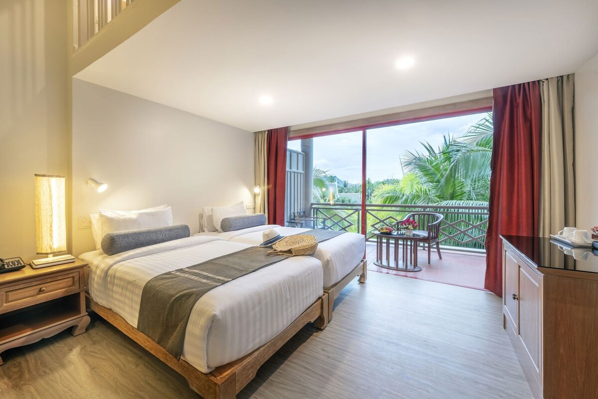 Habitación de hotel con una cama grande, lámparas de noche, un escritorio, una silla y un balcón con vistas a zonas verdes.