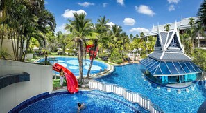 A swimming pool with a water slide, palm trees, and a building with a unique roof design. - Chada Thai Village (Krabi)