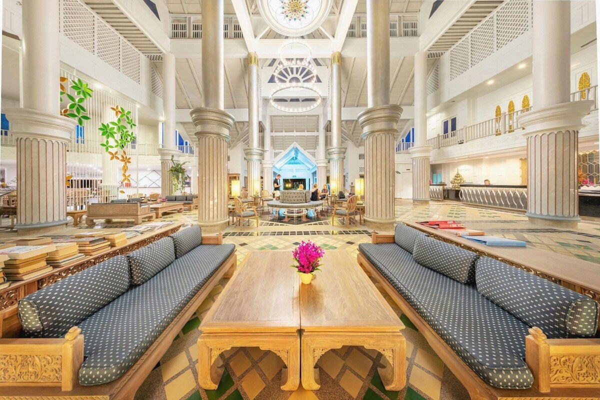 A spacious lobby with high ceilings, ornate columns, and a central seating area with sofas and a coffee table.