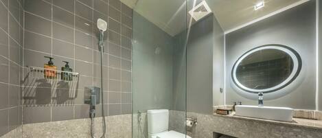 A modern bathroom with a glass-enclosed shower, a toilet, a vanity with a mirror, and a shelf with toiletries.