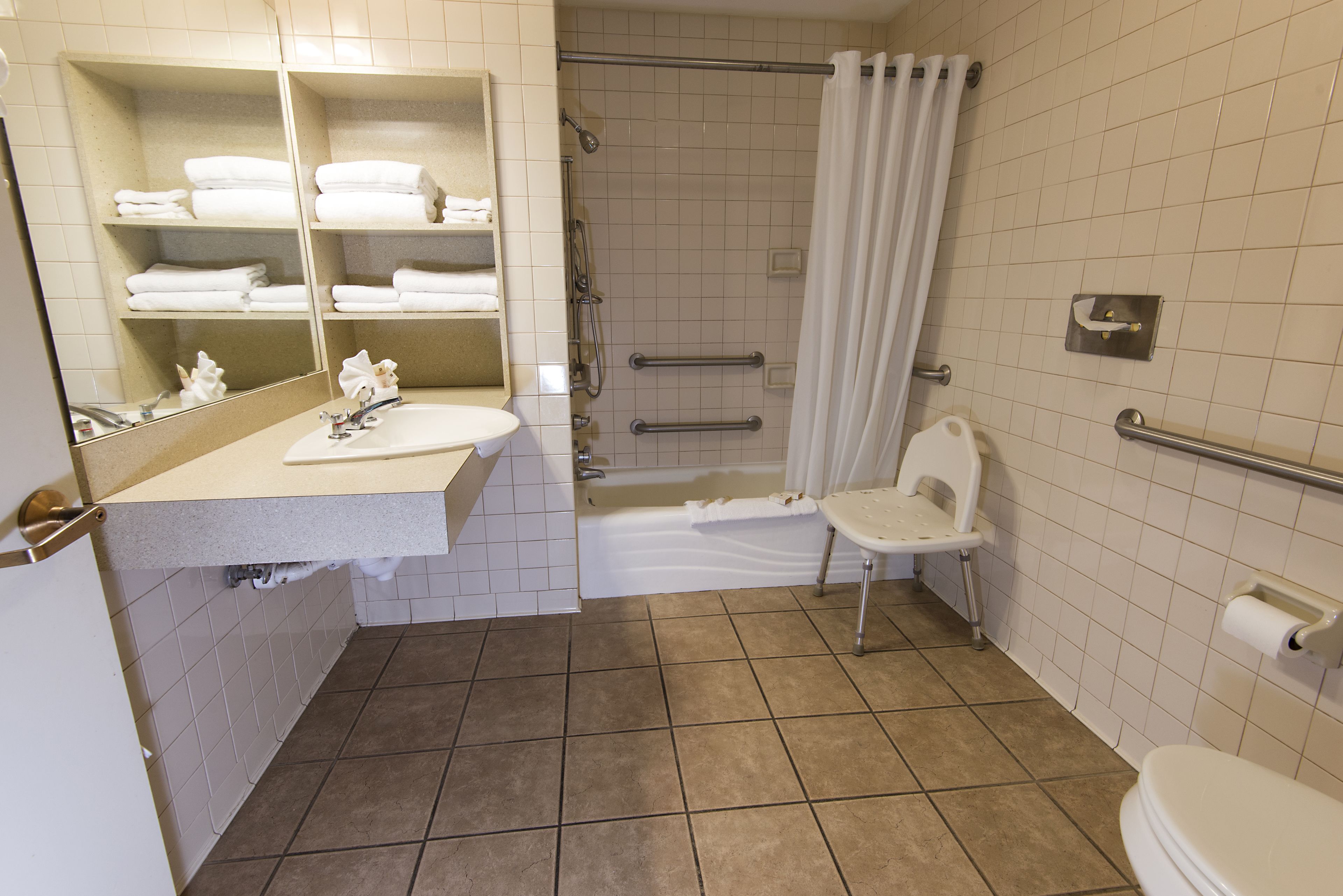 Un baño con lavabo, espejo, toallero, ducha, inodoro y barras de apoyo.