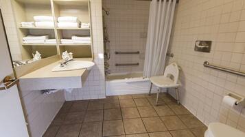Un baño con lavabo, espejo, toallero, ducha, inodoro y barras de apoyo.