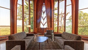 A spacious room with large wooden-framed windows, a central seating area with a sofa and armchairs, and a small table.