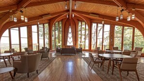 A spacious room with wooden floors and large arched windows, featuring multiple seating areas and tables.