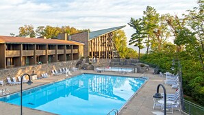 A swimming pool with lounge chairs, a building with a sloped roof, and a stone wall.